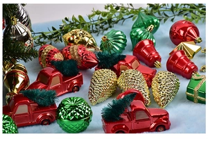 Close-up of red, green, and gold Christmas ornaments including mini truck and pinecone shapes