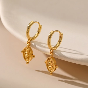 Detailed macro view of gold hoop earrings with snake coin pendants on ceramic