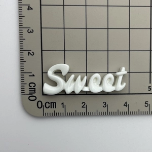 Detailed view of white Sweet resin charm on a grid cutting mat showing 4.5cm size
