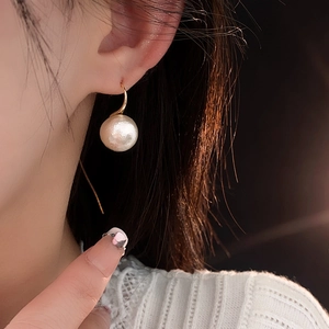 Élégante boucle d'oreille crochet dorée avec perle blanche portée par un mannequin de profil