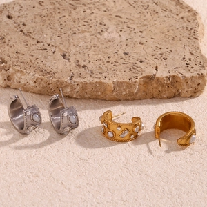 Close-up of gold and silver C-shaped hoop earrings with pearls on a natural stone base