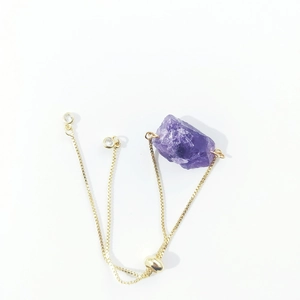 Detailed macro view of the irregular raw amethyst stone on a golden box chain bracelet