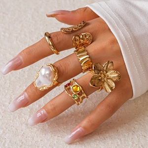 Detailed view of six gold-tone textured rings with pearls and gems on model hand