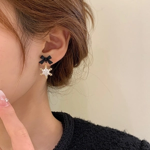 Close-up of elegant Christmas snowflake earrings with black bow and sparkling zircons