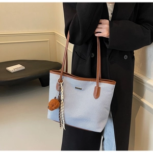 Detail of canvas tote bag featuring brown leather straps and a decorative bear charm