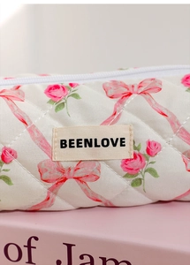 Close-up of quilted floral makeup bag with pink roses and embroidered brand label