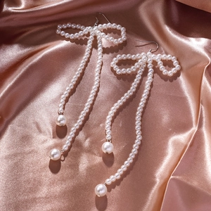 Detail view of bow pearl tassel earrings on elegant rose gold satin background