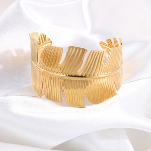 Close-up of golden wide open cuff bracelet with intricate leaf vein texture on white silk