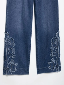 Gros plan sur les broderies effilochées d'un jean bleu foncé avec détails de texture
