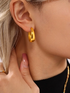 Close-up of minimalist chunky gold oval hoop earrings worn by a model in professional lighting