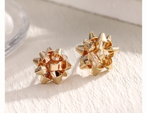 Macro shot of gold ribbon bow earrings with polished finish on beige background