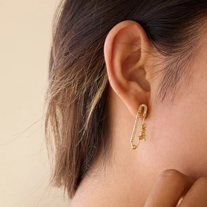 Détail d'une boucle d'oreille trombone dorée avec lettres LOVE et strass blancs brillants