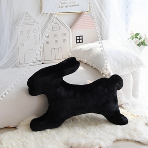 Dettaglio di un morbido cuscino di peluche a forma di coniglio nero su tappeto bianco
