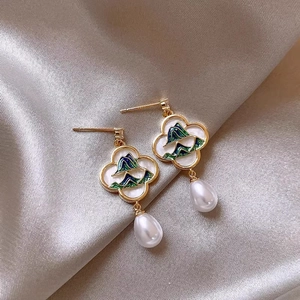 Macro view of French style gold earrings with mountain enamel and drop pearl accents