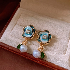 Macro detail of blue flower earrings with pearls and green leaves on velvet