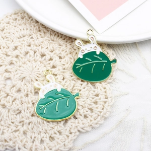 Detail shot of cute white rabbit enamel charms behind green leaves on crochet mat
