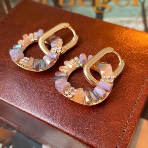 Baroque style gold hoop earrings with purple crystals and zircons on a leather jewelry box