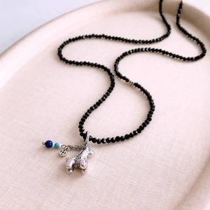 Close-up of black faceted beads with a silver horse pendant and traditional coin charm