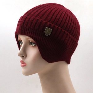 Close-up of wine red ribbed knit beanie with ear flaps and metallic shield logo