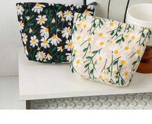 Detail of daisy embroidery on black and cream canvas makeup bags in a home setting