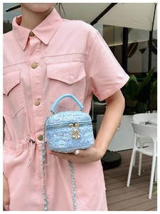 Detail of blue sequined mini bag with metal chain strap and top handle held by a model