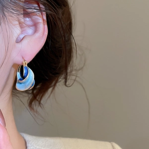Detail of twisted gold hoop earrings with gradient blue enamel on female model