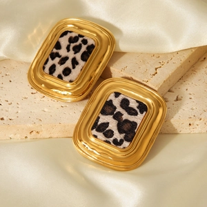 Détail de boucles d'oreilles en acier doré 18K avec motif léopard sur soie beige