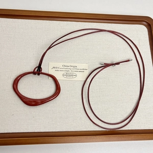 Close-up of red organic shape pendant on long cord displayed on linen board