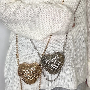 Detailed view of heart-shaped hollow metal chain bag worn over a white knit sweater