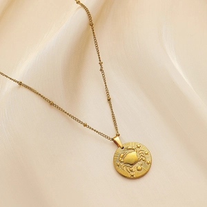 Detail shot of golden Cancer zodiac coin necklace with crab relief on beige silk