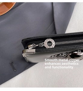 Detailed macro of smooth black leather wallet featuring a textured silver logo zipper