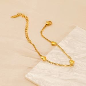 Vista detallada de una pulsera con dijes de corazón dorado sobre mármol blanco
