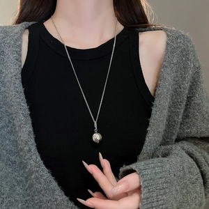 Detail of silver bead pendant on fine chain necklace worn by a model in casual attire