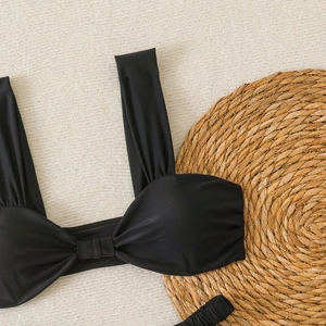 Détail du haut de bikini noir avec nœud plissé et larges bretelles sur fond de plage d'été