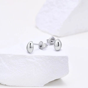 Macro detail of high-polished silver bean earrings on textured stone background