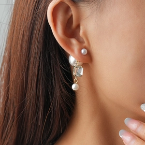 Detail shot of double-layered pearl earrings with a rectangular crystal pendant and gold finish