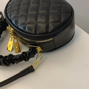 Detailed macro shot of a black quilted round crossbody bag with gold zippers and metal.