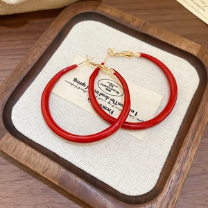 Detail of red enamel hoop earrings with gold hooks on a vintage wooden tray display