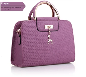 Detail of purple pebble leather handbag with gold deer charm and round metal handle