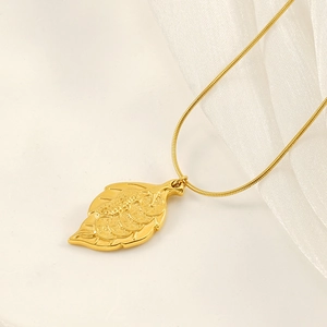 Minimalist gold leaf pendant necklace with peanut relief detail on white silk fabric