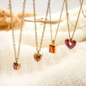 Close-up of gold necklaces with red heart-shaped and rectangular zircon pendants on white knit