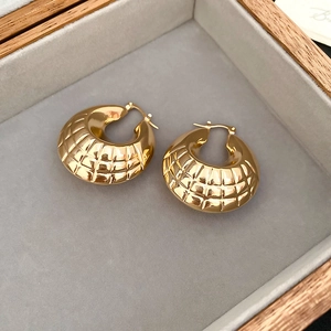 Macro shot of gold hoop earrings with quilted texture in a grey velvet jewelry box