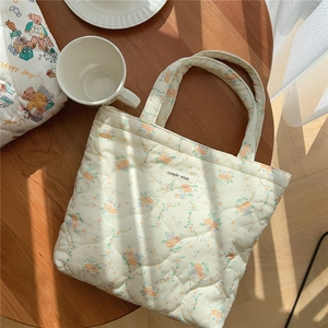Détail d'un sac à main matelassé à fleurs avec étiquette posé sur une table en bois
