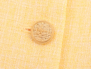 Dettaglio ravvicinato di un bottone dorato su tessuto tweed giallo intrecciato