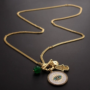 Gold Hamsa Hand and Evil Eye pendant necklace with green bead on black background