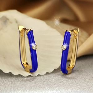 Detail of gold U-shaped earrings with royal blue enamel and sparkling zircon on a shell