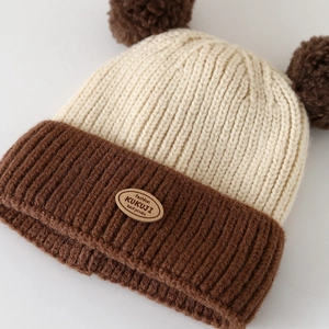 Detail of baby knit hat showing dual pom-poms and soft bi-color woven texture