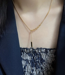 Detail of a minimalist gold bar pendant on a titanium steel necklace worn by a model