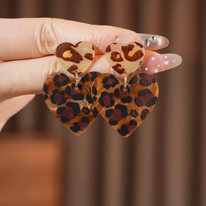 Detailed view of leopard print heart earrings held by a model for a stylish retro look