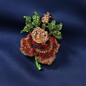 Vintage rose flower brooch with sparkling rhinestones and green leaves on silk background